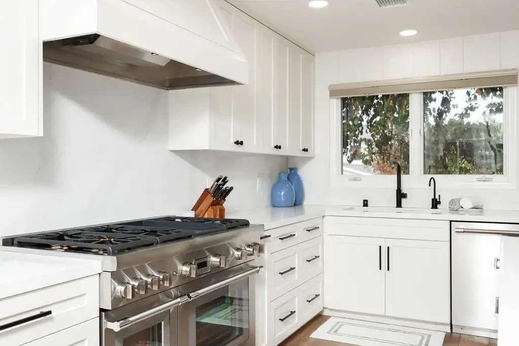 Professional stainless range under stainless hood in white shaker kitchen