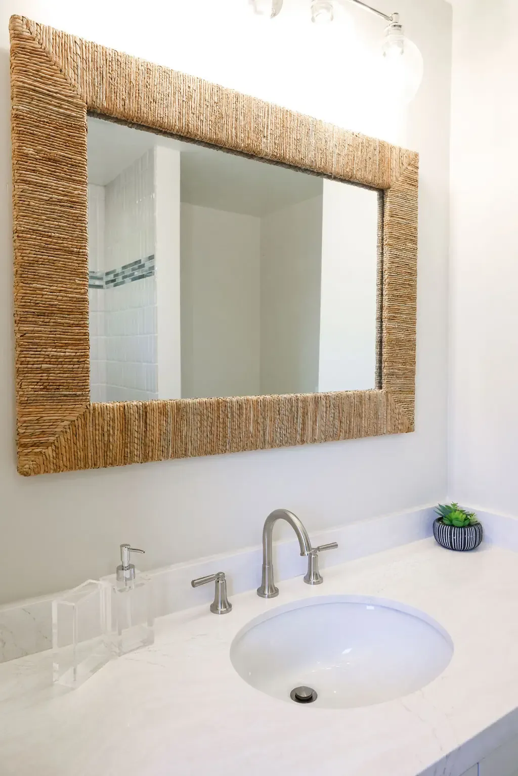 Remodeled bathroom vanity with woven rope-framed mirror and white quartz countertop