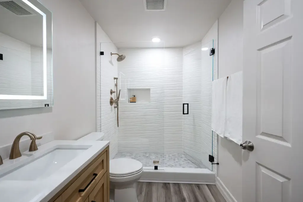 Remodeled bathroom with glass shower, white quartz vanity and gray wood flooring