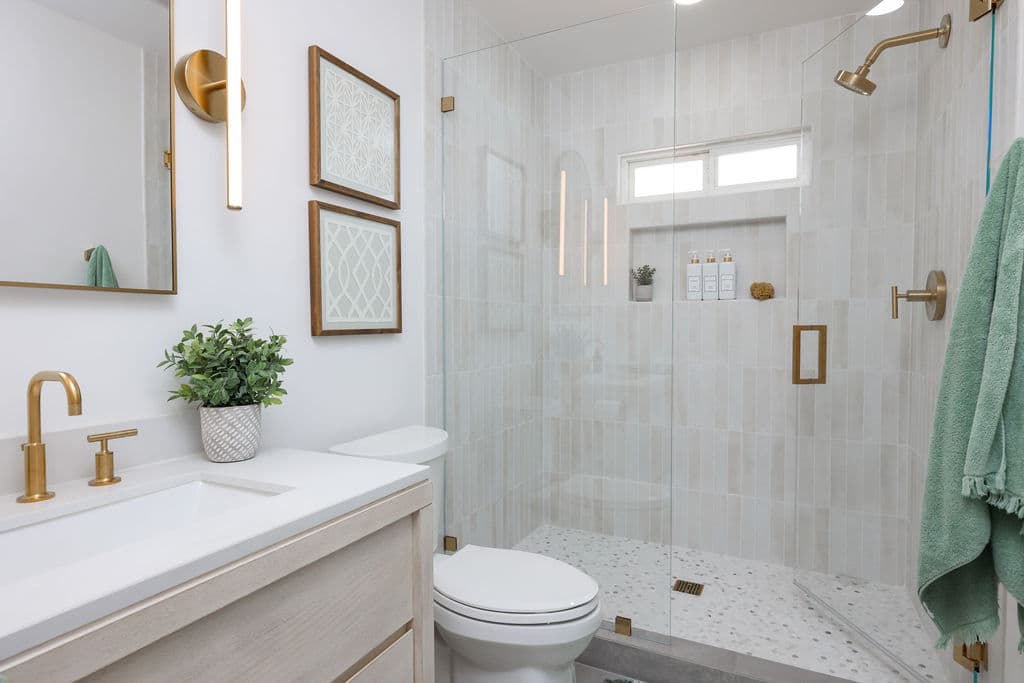remodeled bathroom with glass walk-in shower, light oak vanity and brass fixtures