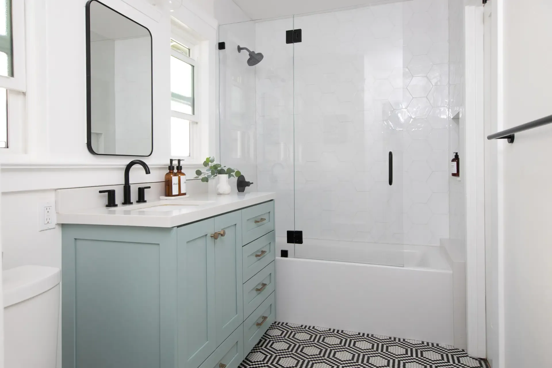 Remodeled bathroom with sage green vanity, glass shower and geometric mosaic floor tile