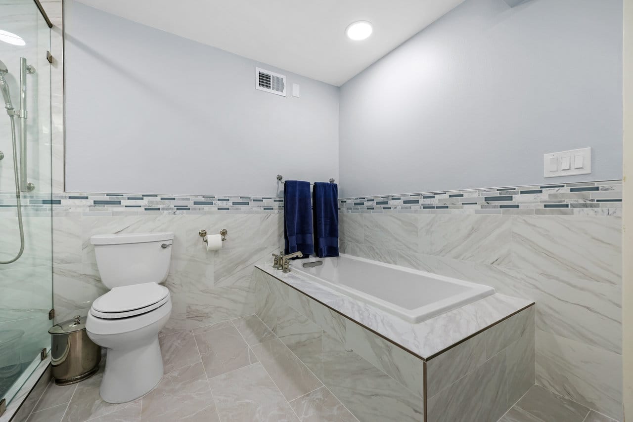 remodeled bathroom with white drop-in soaking tub and marble-look tile with glass mosaic accent band