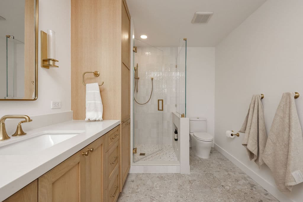 Remodeled bathroom with white oak vanity, glass shower, and marble mosaic floor