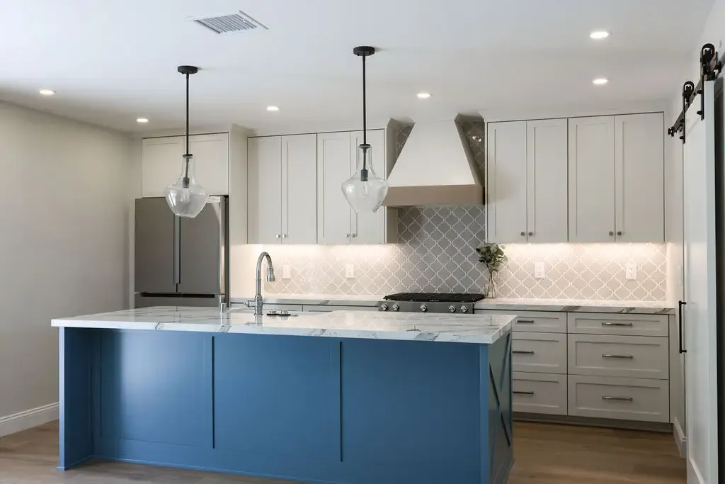 Remodeled kitchen with blue island, white shaker cabinets and arabesque tile backsplash