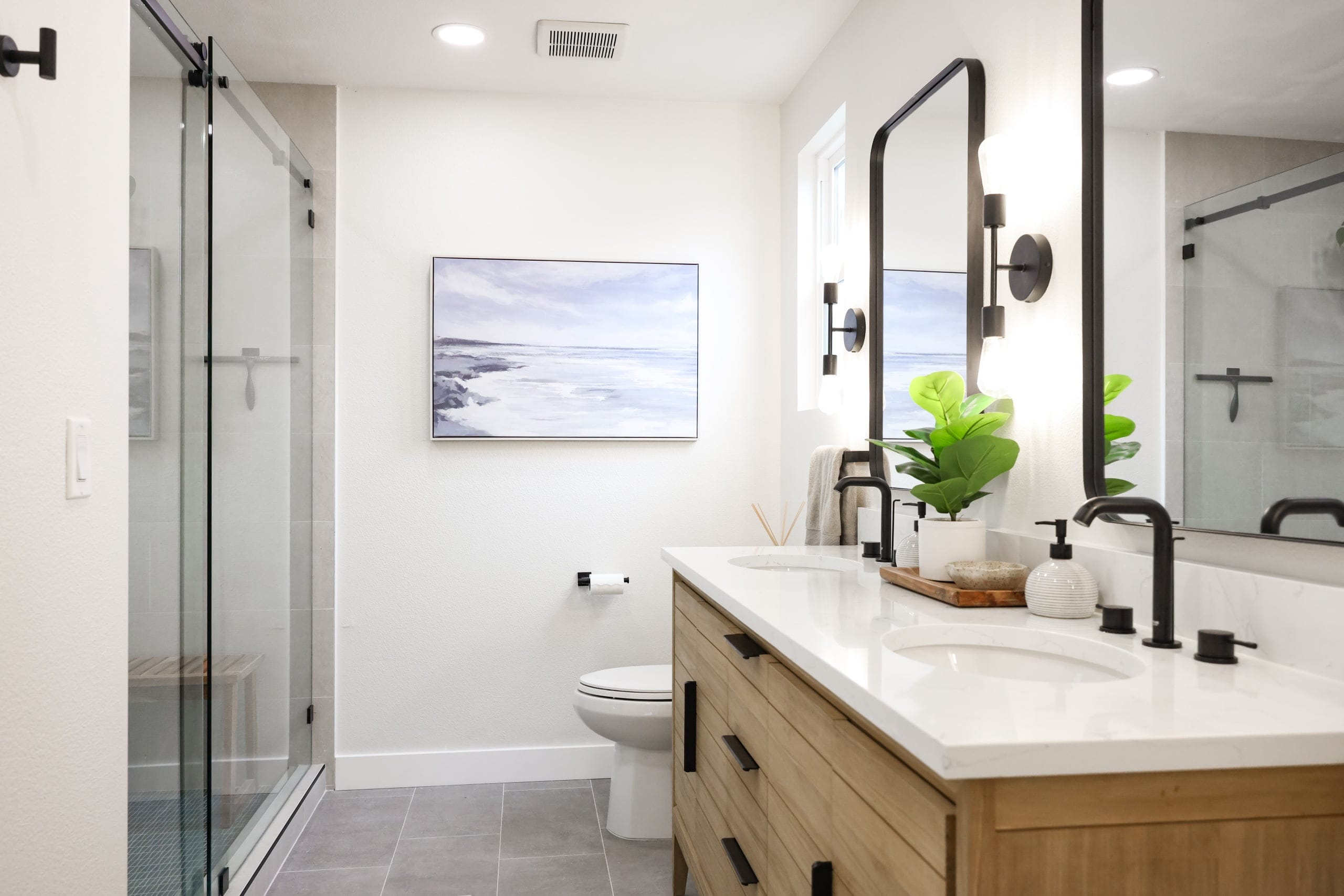 Remodeled primary bathroom with double quartz vanity, oak cabinetry and walk-in glass shower