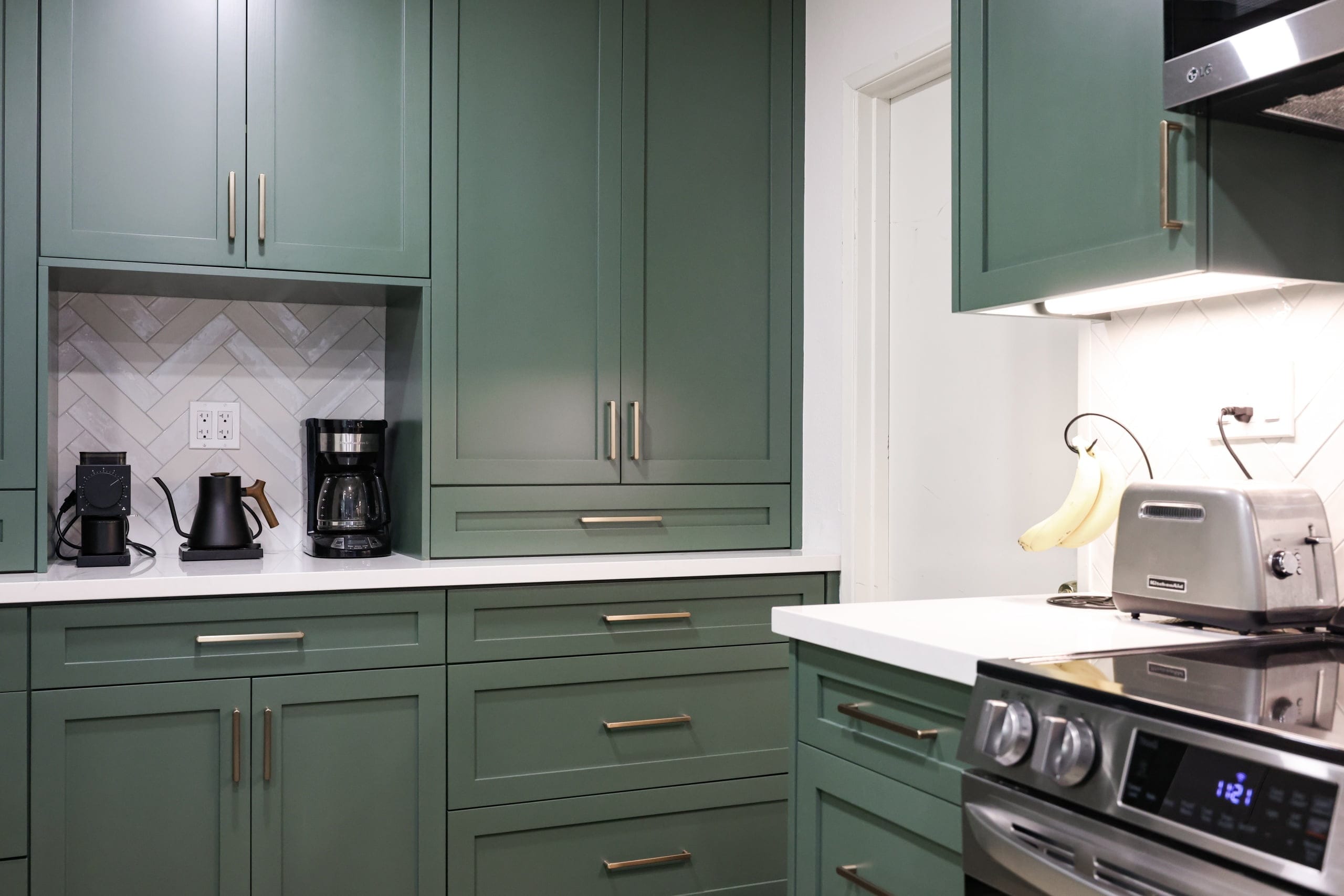 Sage green kitchen with brass pulls, coffee niche and stainless electric range with toaster
