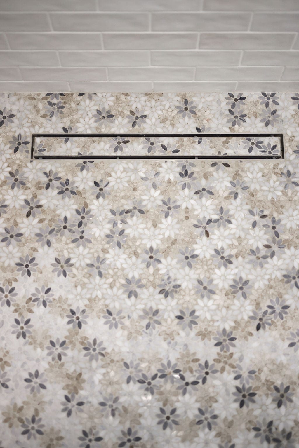 Shower floor with floral gray and cream mosaic tile and linear drain