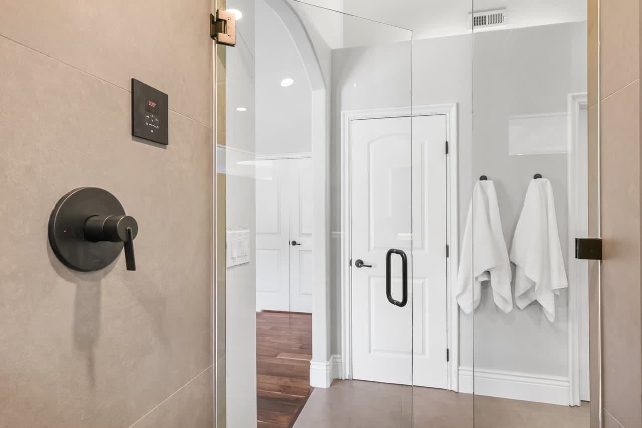 shower interior view through glass toward white paneled door and arched hallway