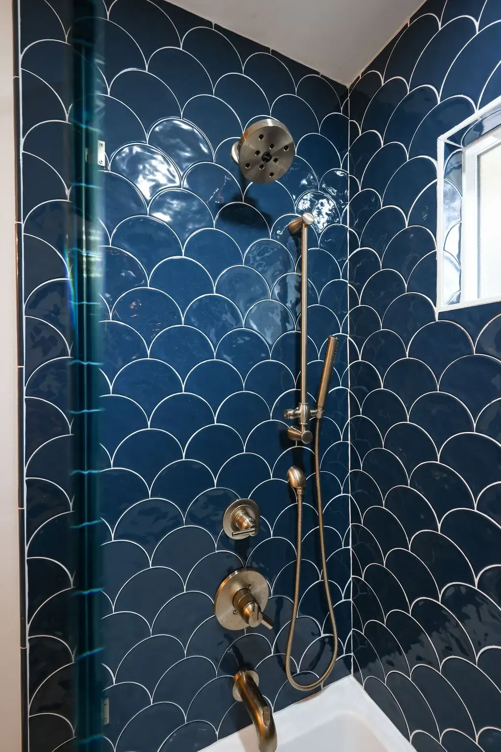 Shower wall in glossy blue scallop tile with brushed gold fixtures and handheld sprayer