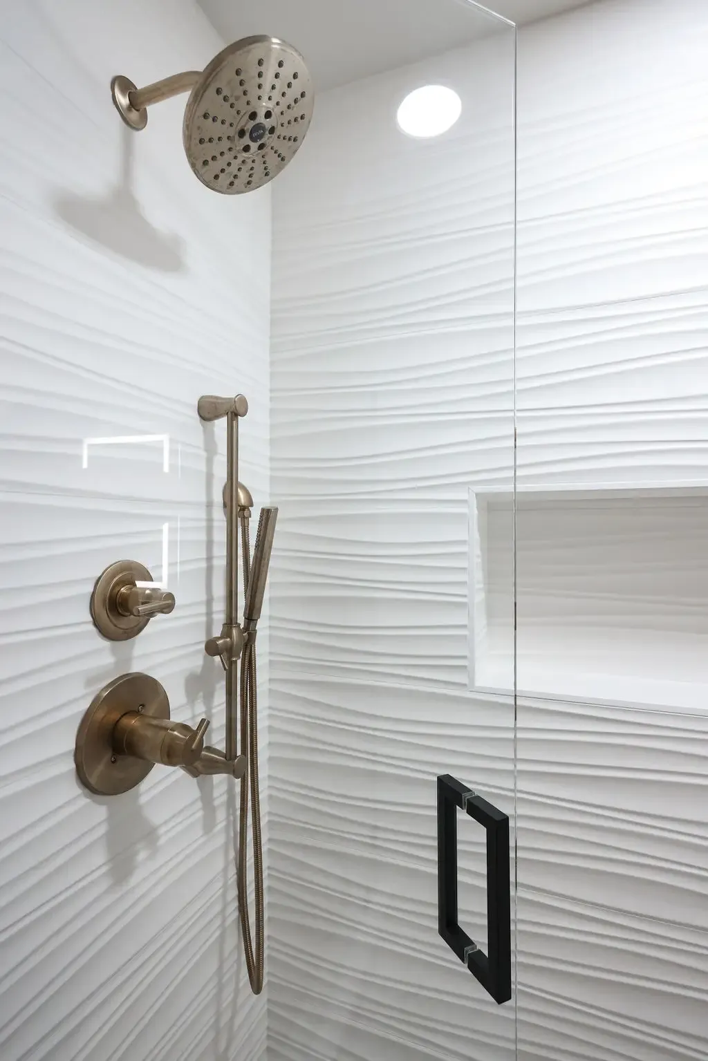 Shower wall in rippled white tile with brushed bronze rainfall head and slide bar