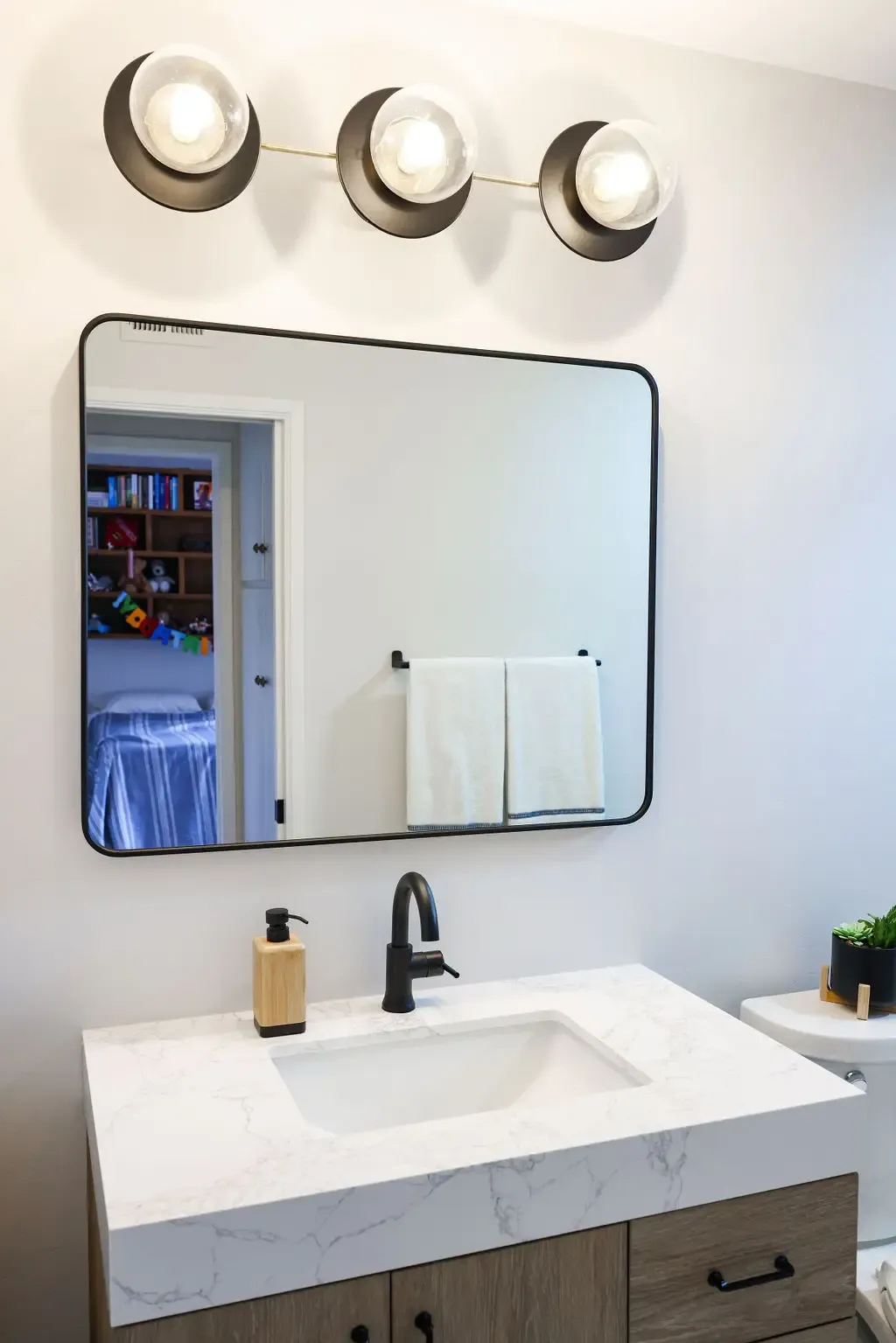Single vanity bathroom with marble counter, black faucet and three-bulb light fixture