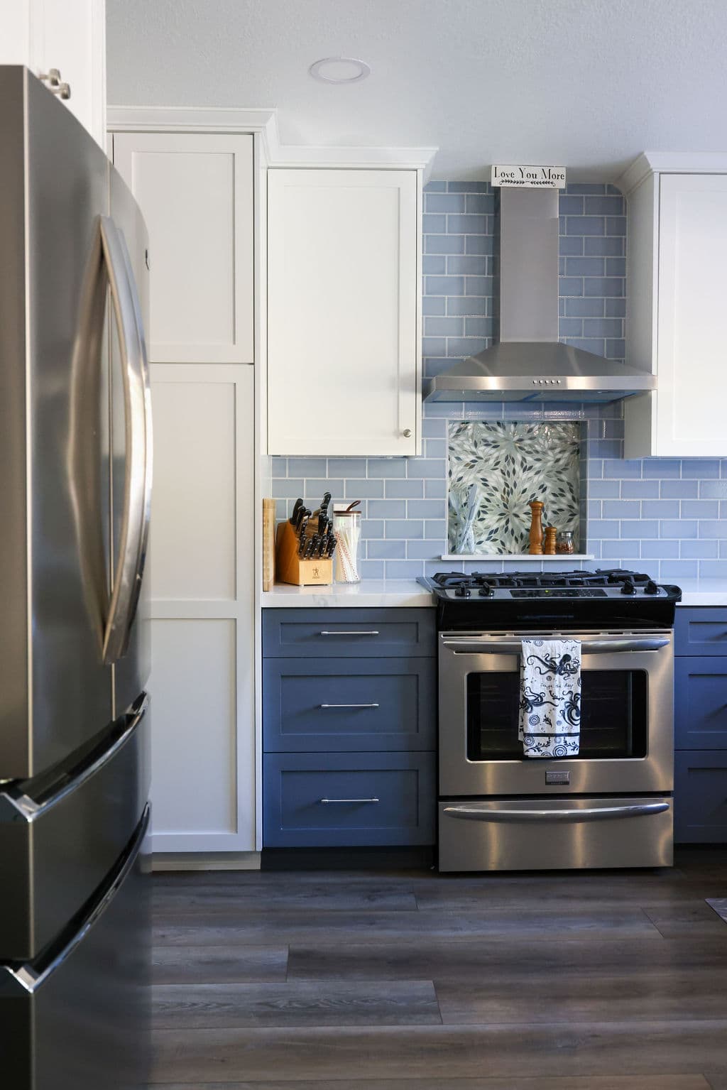 Slide-in range with stainless hood, floral mosaic niche and two-tone cabinetry