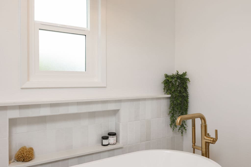 Soaking tub corner with brass filler, white zellige tile, and recessed niche