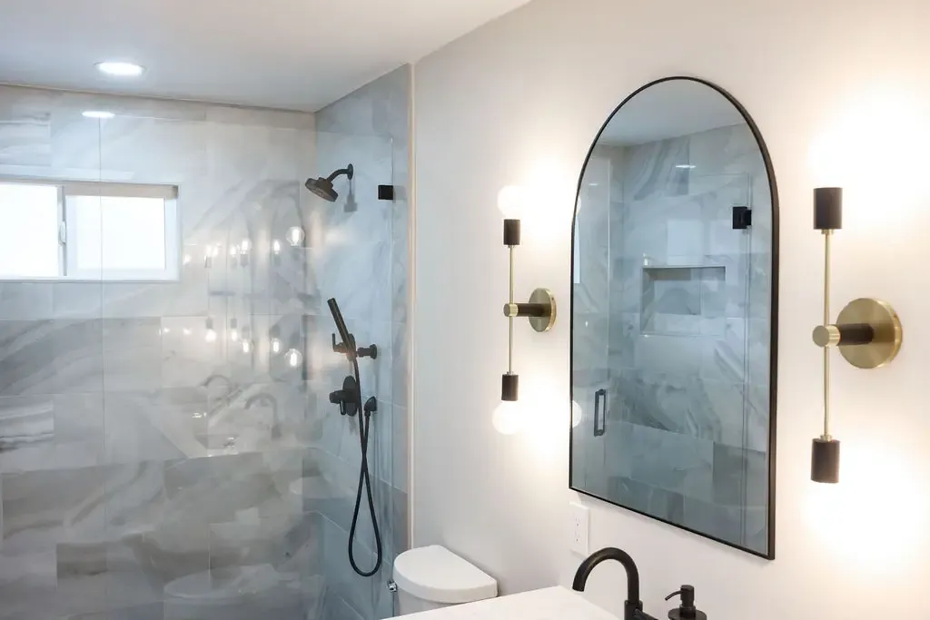 Spa-style bathroom featuring brass sconces, arched black mirror and tiled glass shower