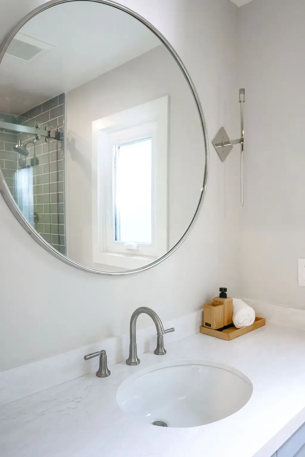 Spa-style bathroom vanity with circular mirror and marble counter near glass shower