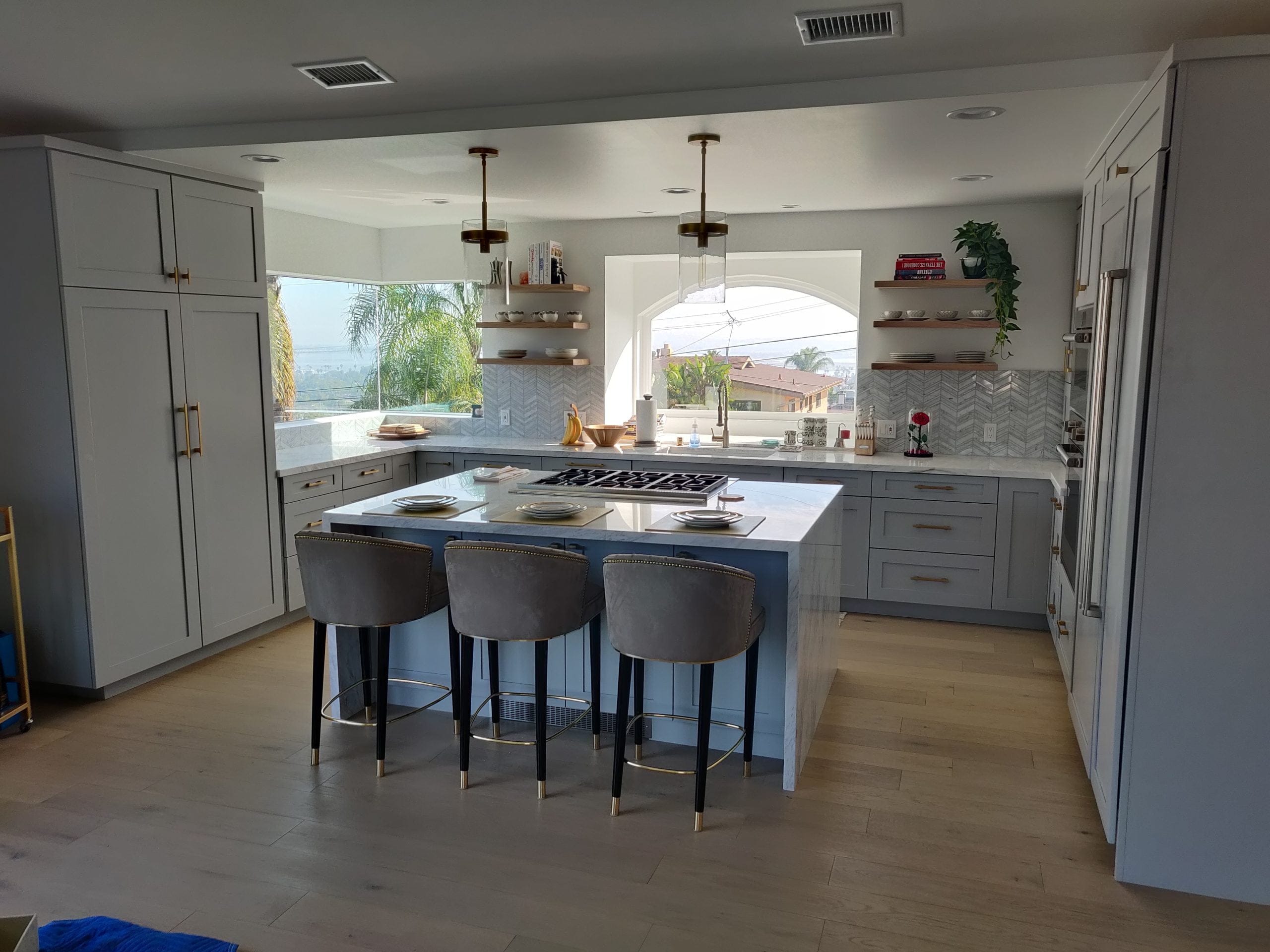 spacious gray kitchen with marble island, velvet barstools, and arched view windows