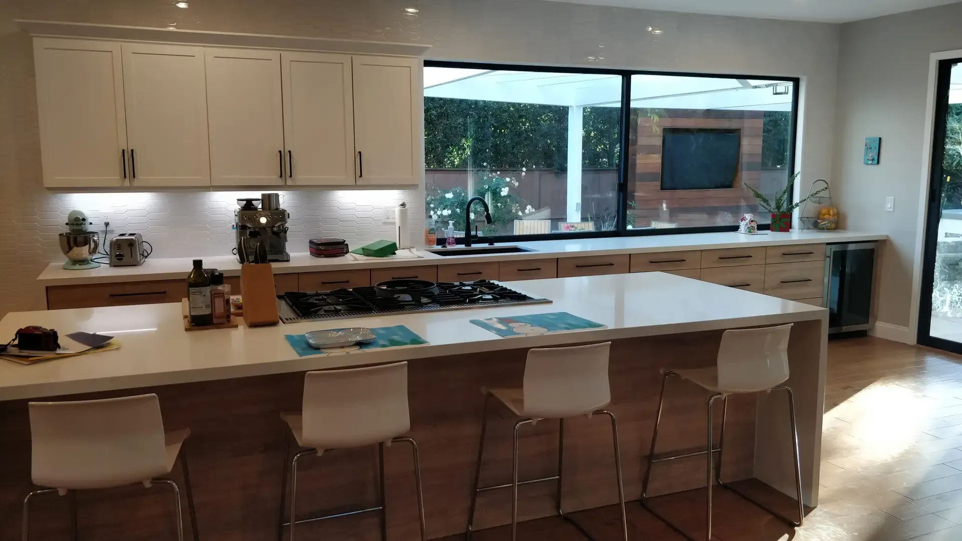 Spacious kitchen with long quartz island, bar stools and panoramic backyard window