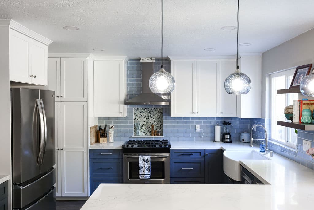 Spacious kitchen with white and navy cabinets, quartz island and mercury-glass pendants