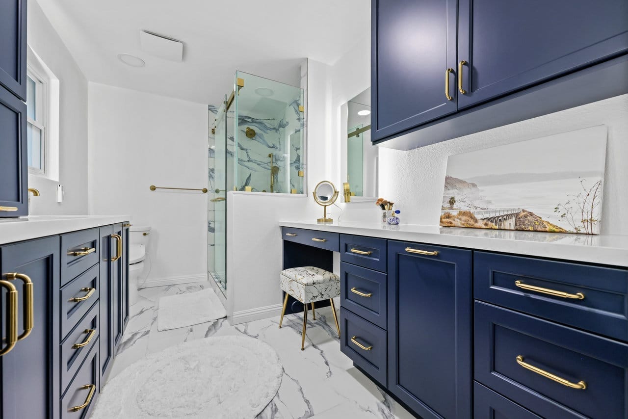 Spacious primary bath with navy cabinetry, gold hardware and marble-look tile floor