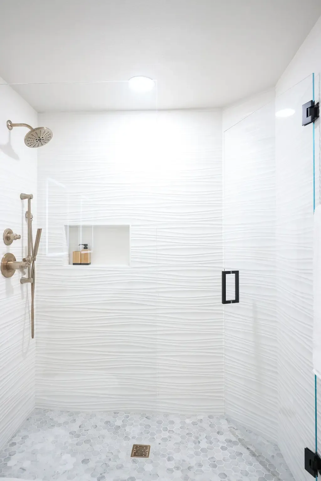 Spacious walk-in shower with white ribbed tile, marble mosaic floor and glass surround