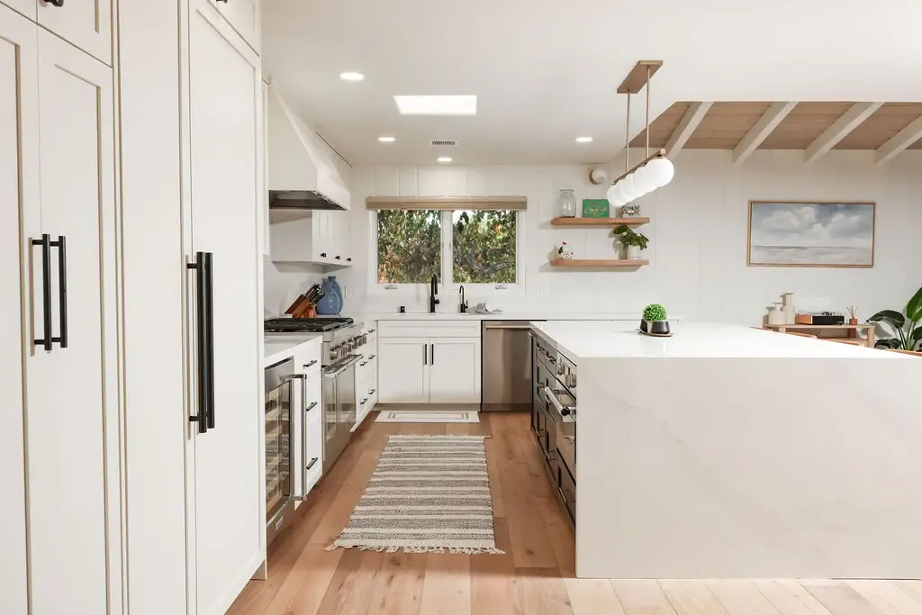 Spacious white kitchen with waterfall quartz island, range hood and oak flooring