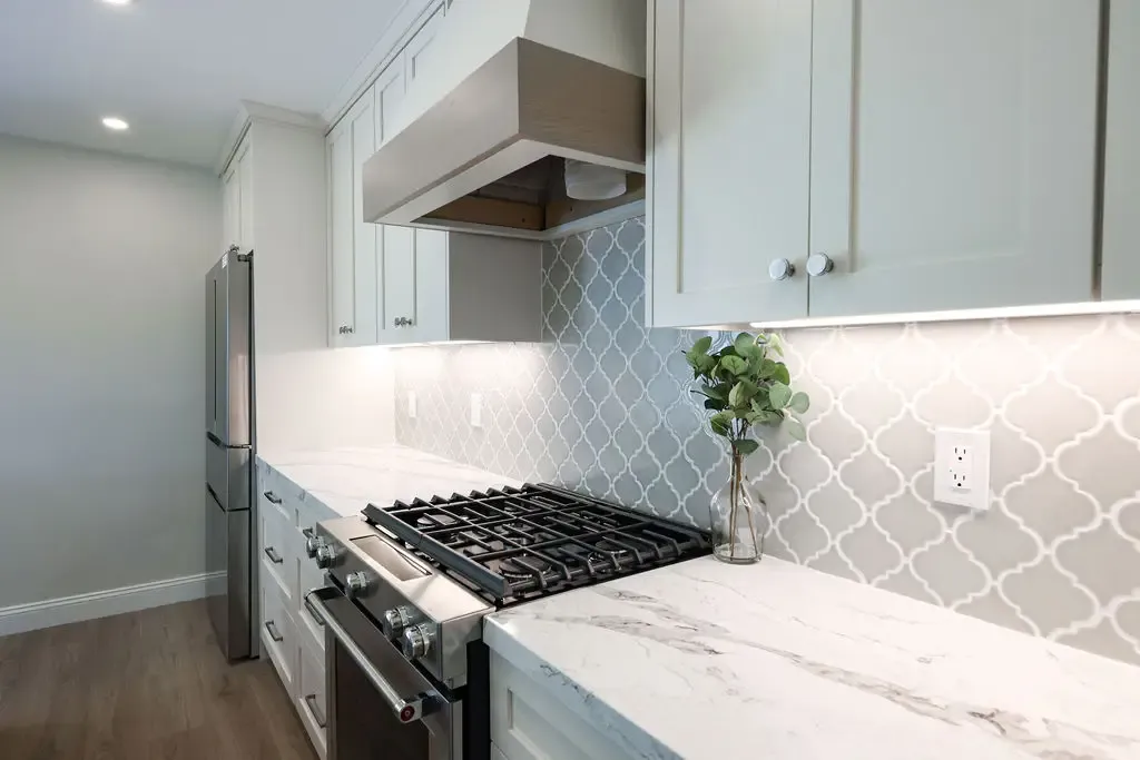 Stainless gas range flanked by marble counters under arabesque tile backsplash