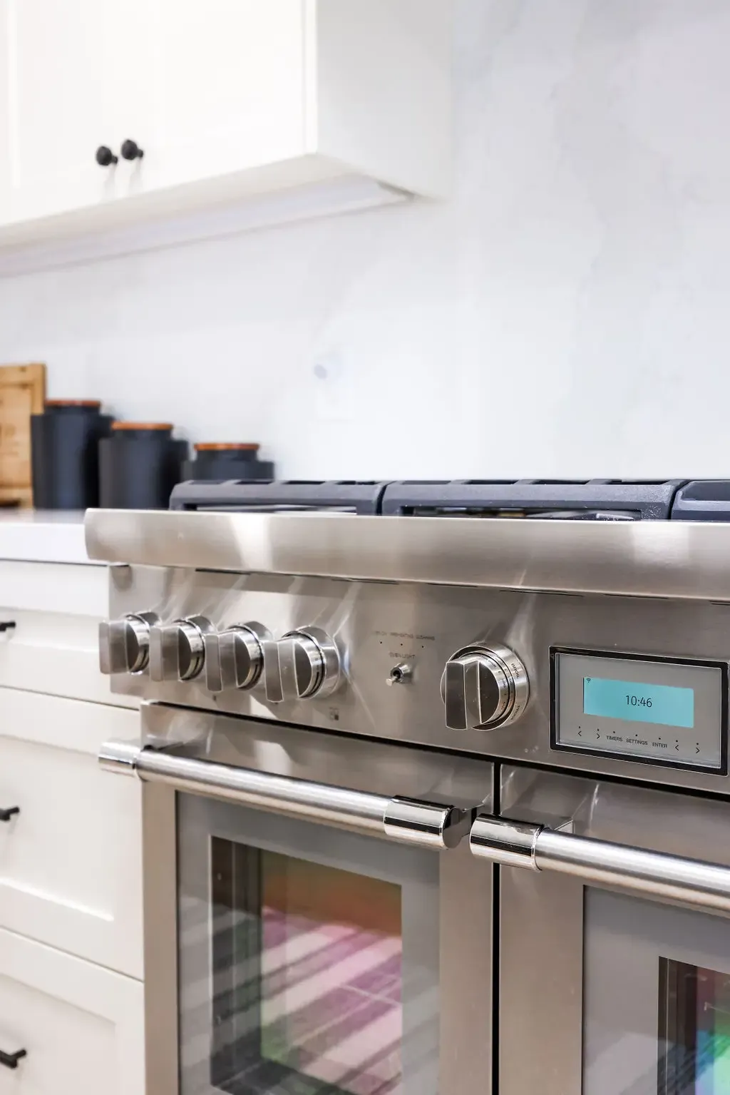 Stainless pro range detail with control knobs beside white cabinetry