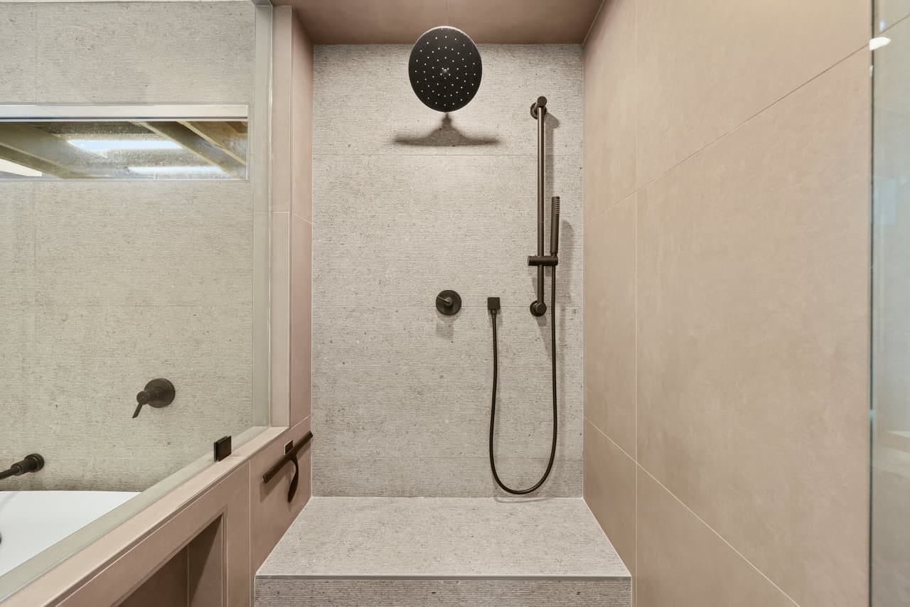 stone-tiled walk-in shower with bronze rain head, handheld sprayer and bench