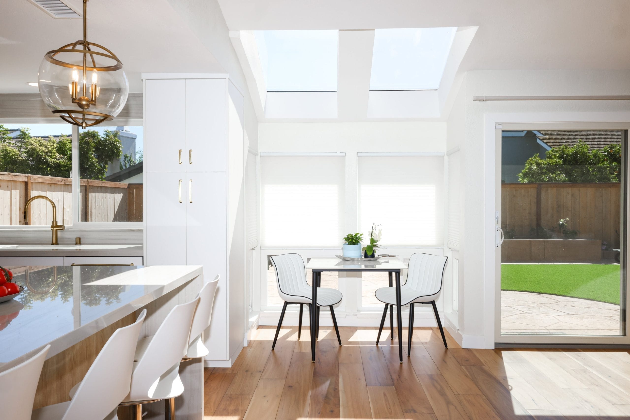Sunlit breakfast nook with skylights, white chairs and sliding door to yard