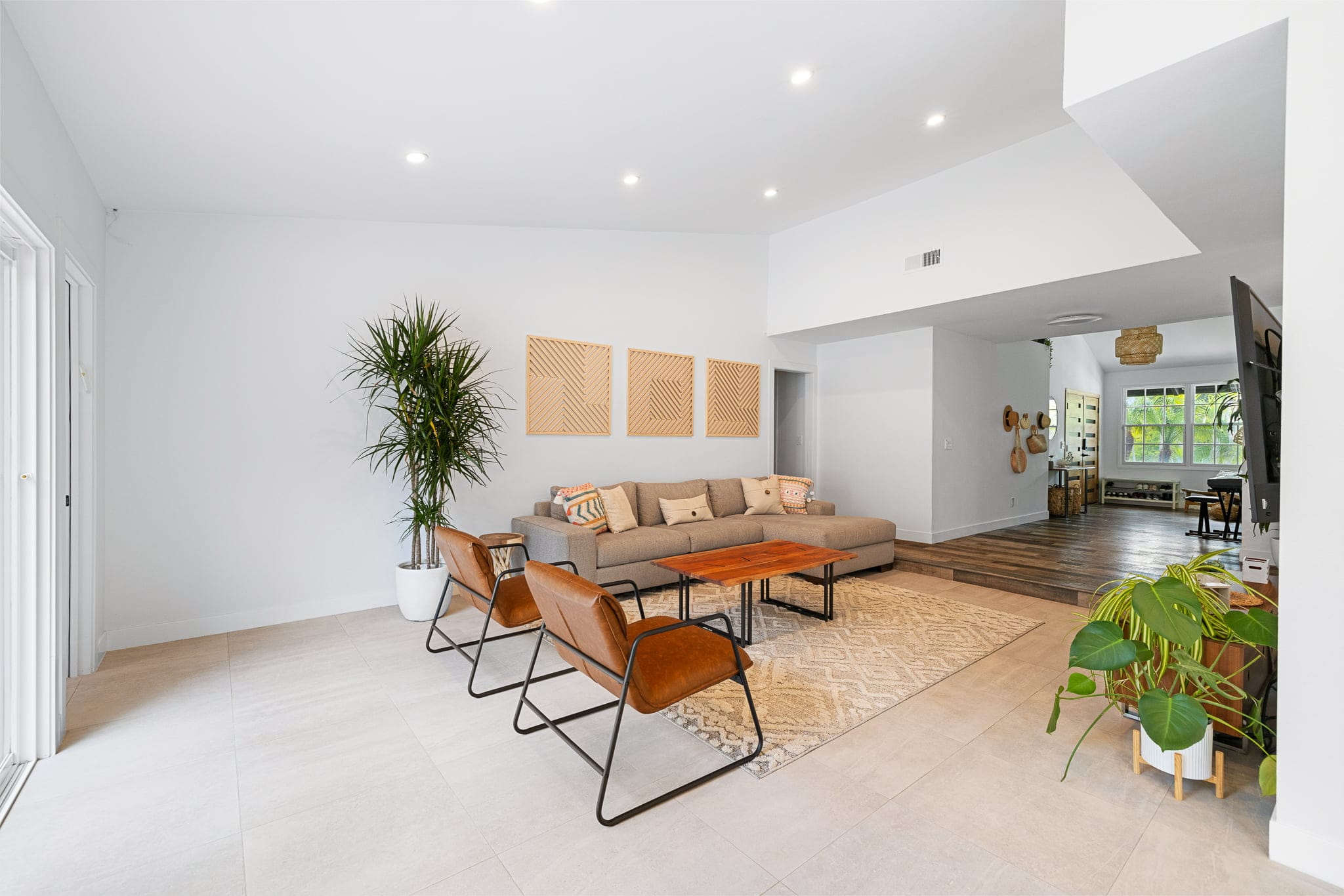 Sunlit lounge with leather chairs, tall plant and tile-to-wood flooring transition