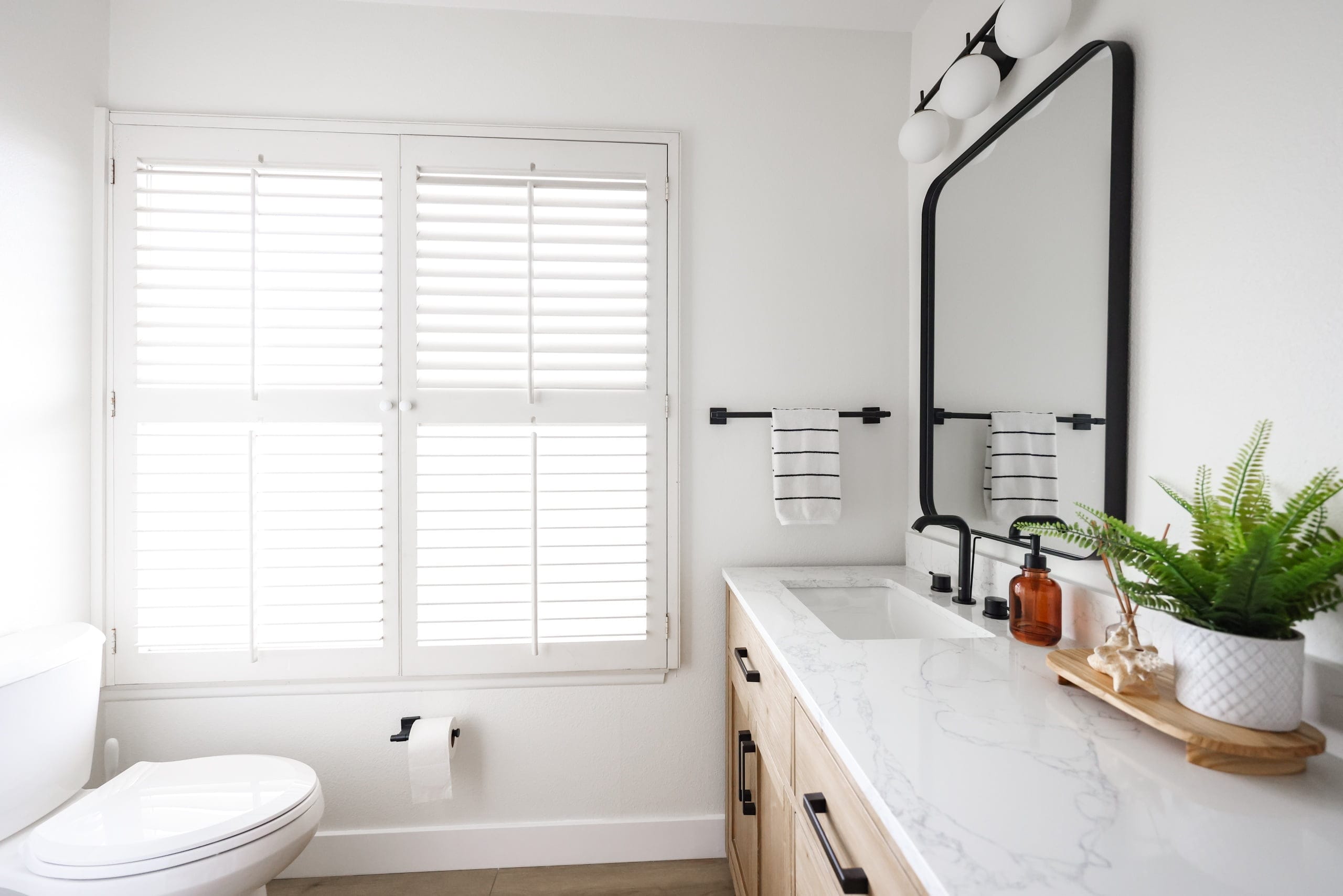 Sunny bathroom with plantation shutters, marble counter, and oak cabinetry