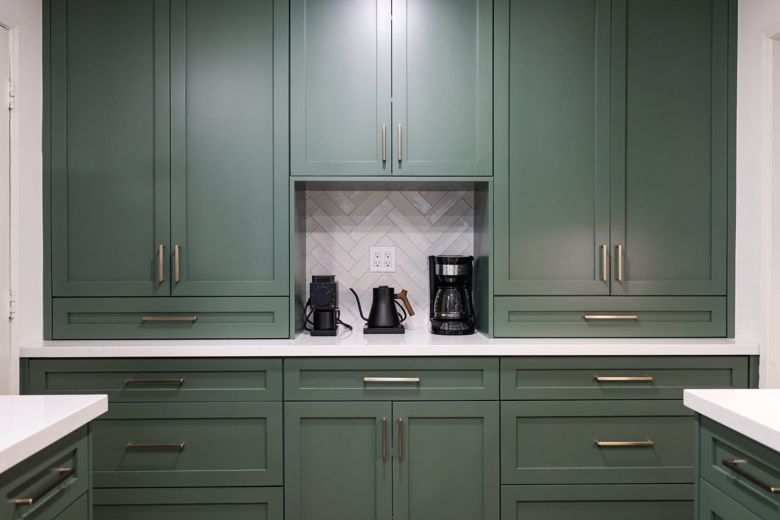 Symmetrical green cabinetry wall with quartz counters and herringbone-tiled appliance nook