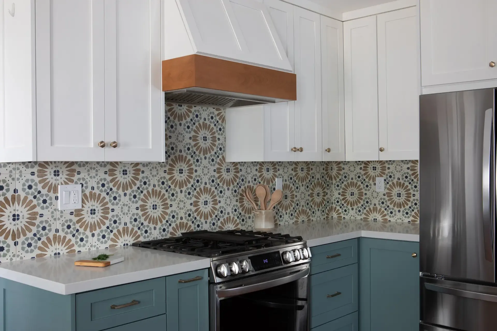 Teal-and-white kitchen with wood-trimmed range hood and bold floral-pattern tile backsplash