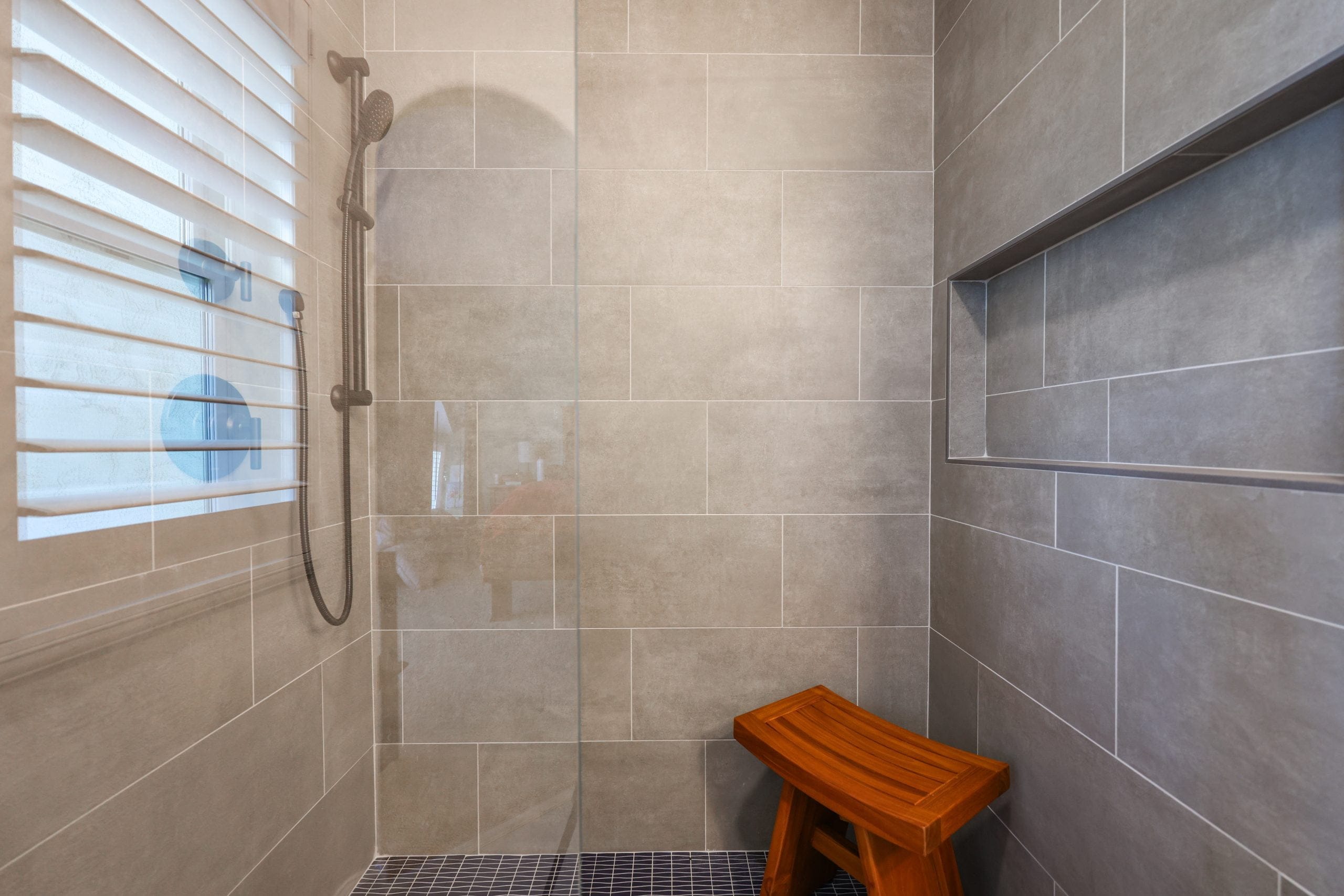 Tiled shower featuring handheld sliding bar, long recessed shelf and wooden bench