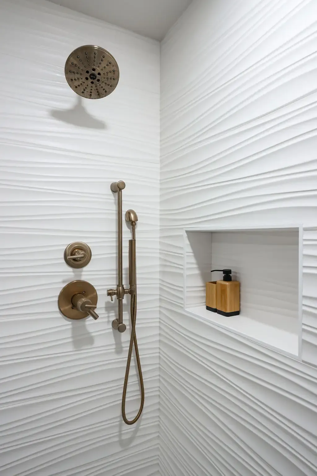 Tiled shower featuring rippled white wall tile, aged bronze rainfall head and shelf niche