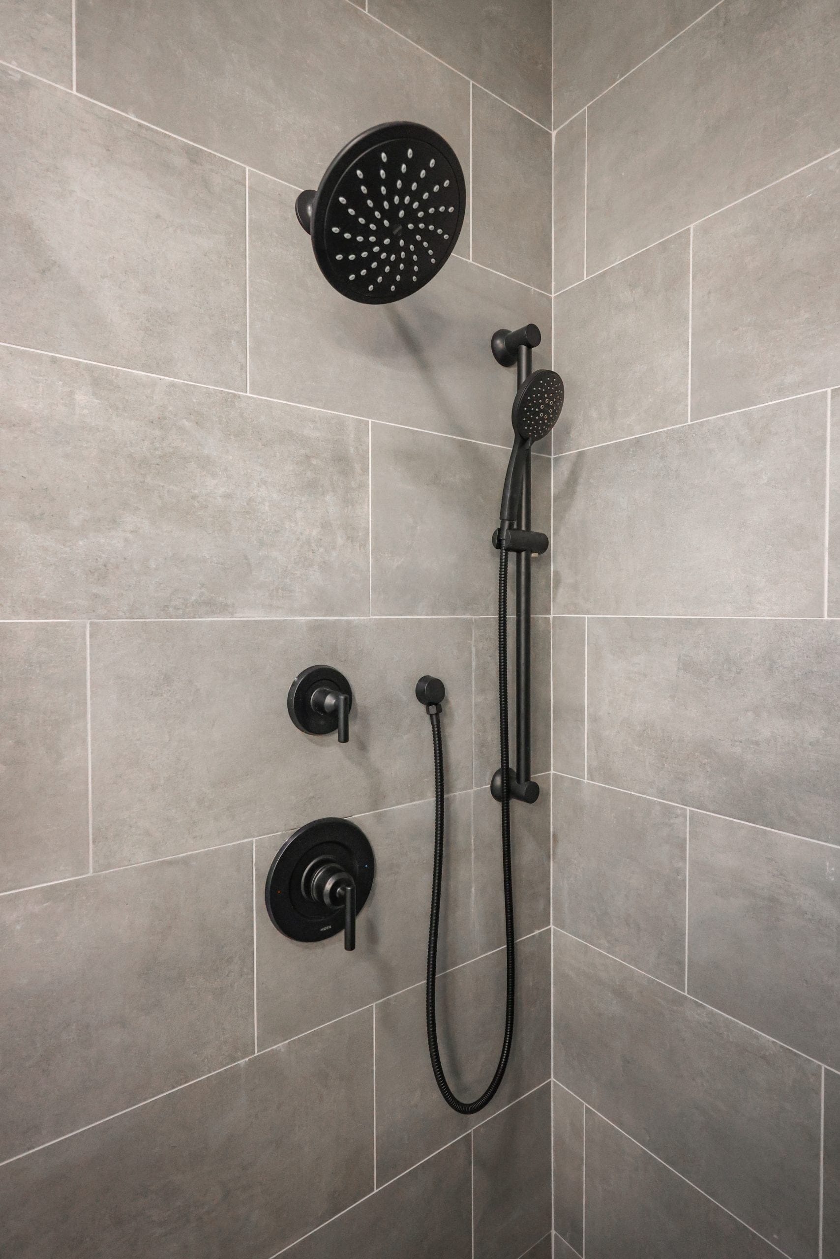 Tiled shower in gray large-format tile with matte black showerhead and handheld