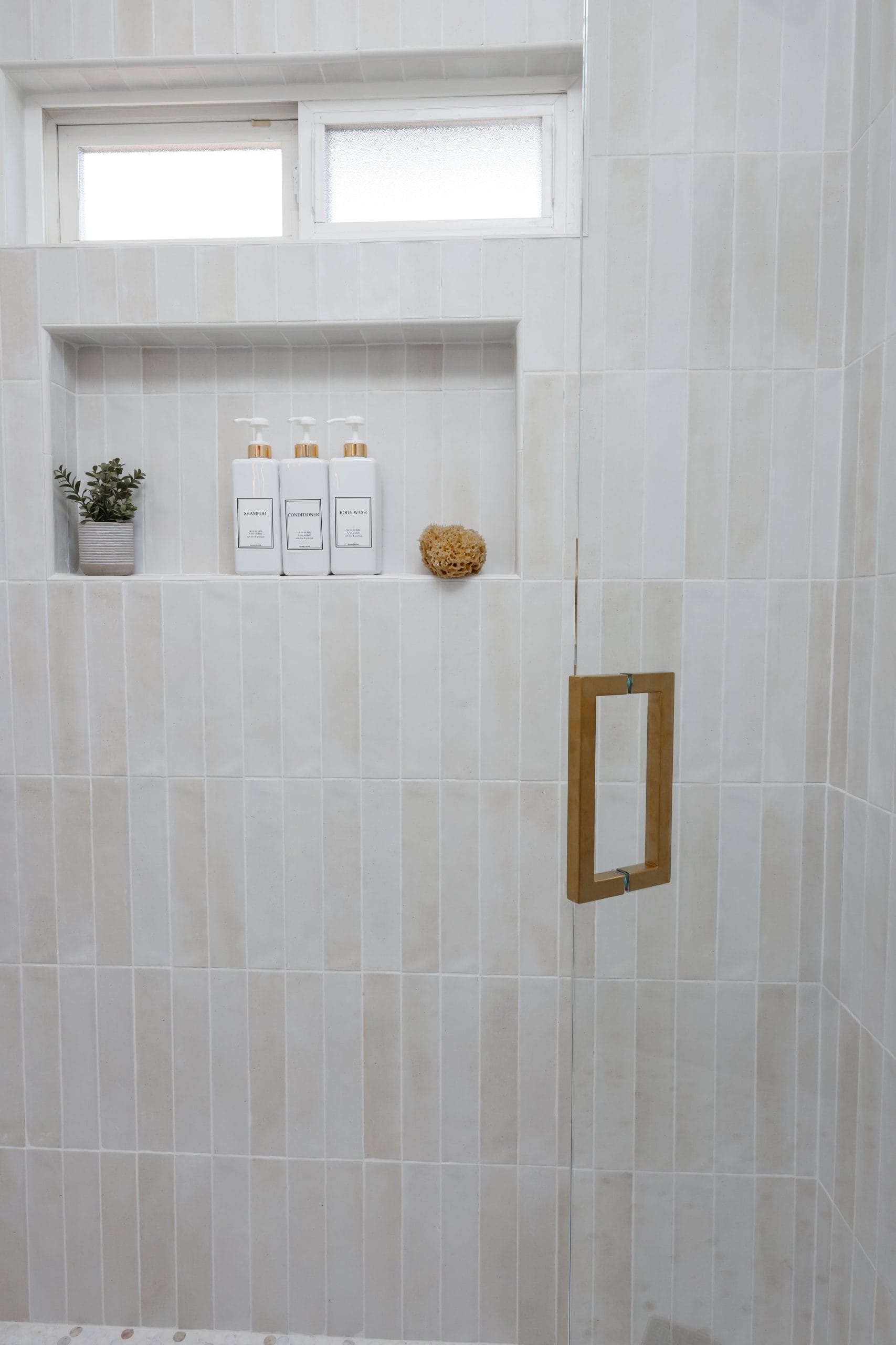 tiled shower interior with recessed niche, frosted window and warm brass glass-door handle
