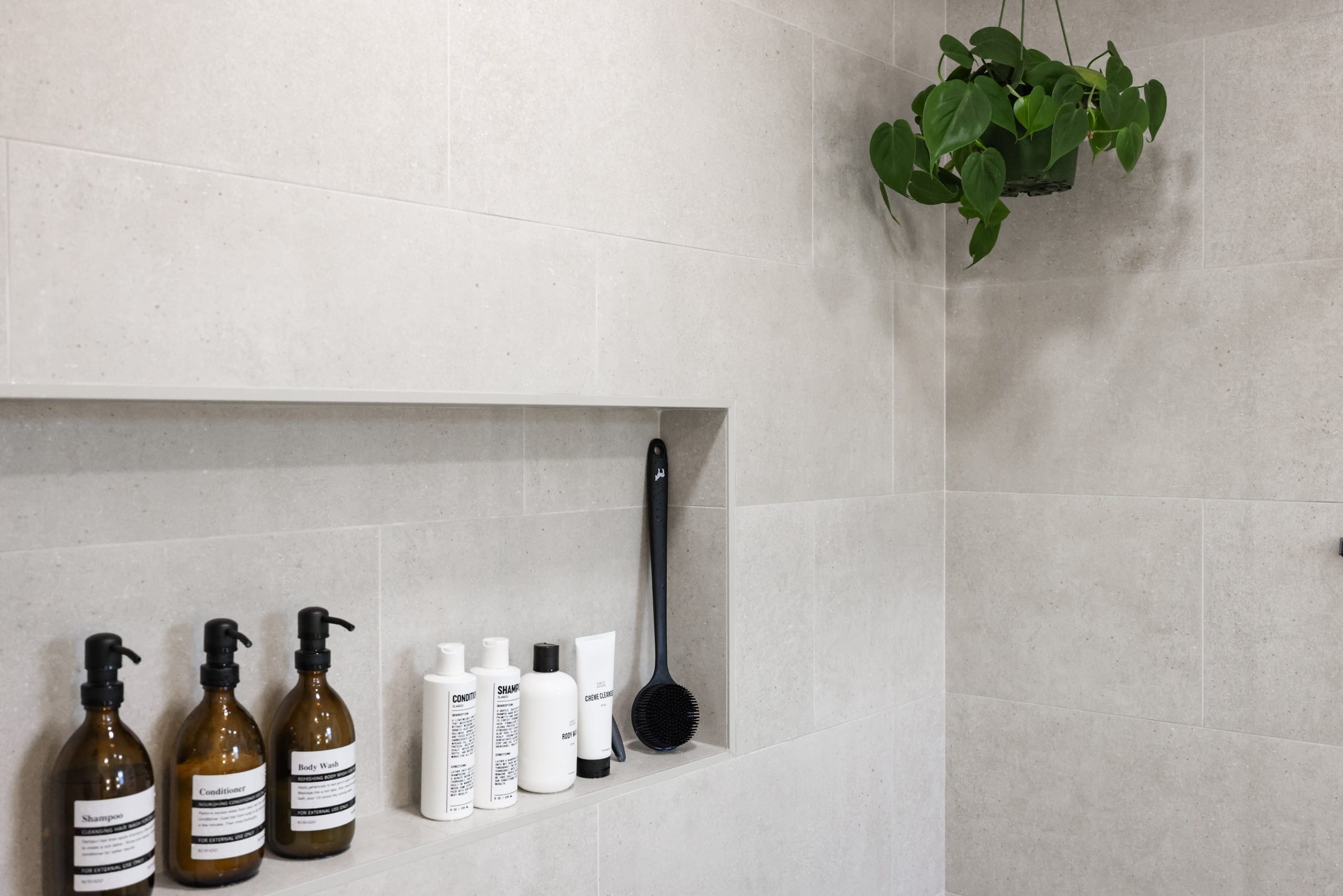 Tiled shower niche holding amber bottles beneath a hanging trailing plant