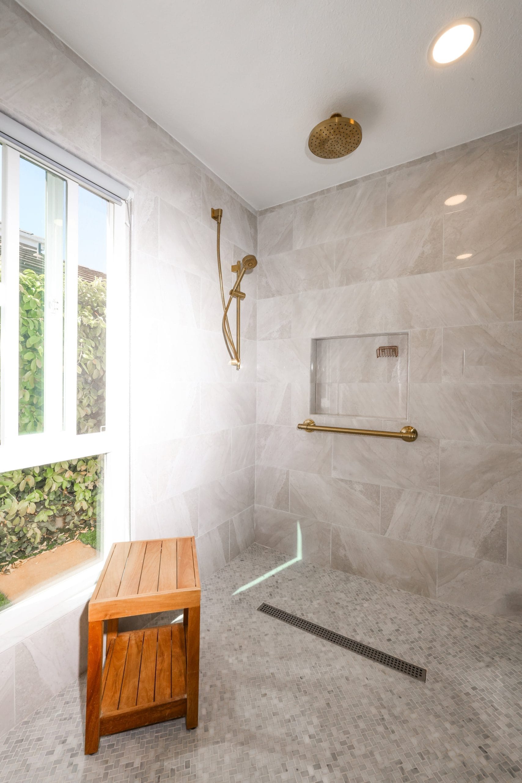 Tiled walk-in shower with brass rainfall fixtures, teak bench and linear drain
