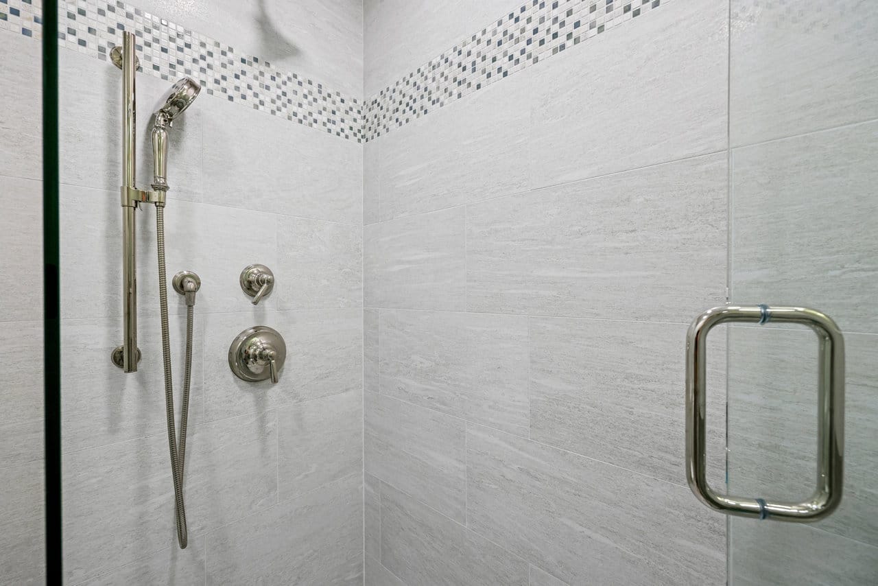 Tiled walk-in shower with mosaic accent border, handheld fixture and frameless glass door