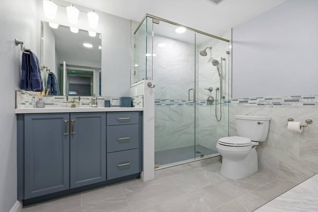 transitional bathroom with gray vanity, frameless glass shower, marble tile and brushed nickel fixtures