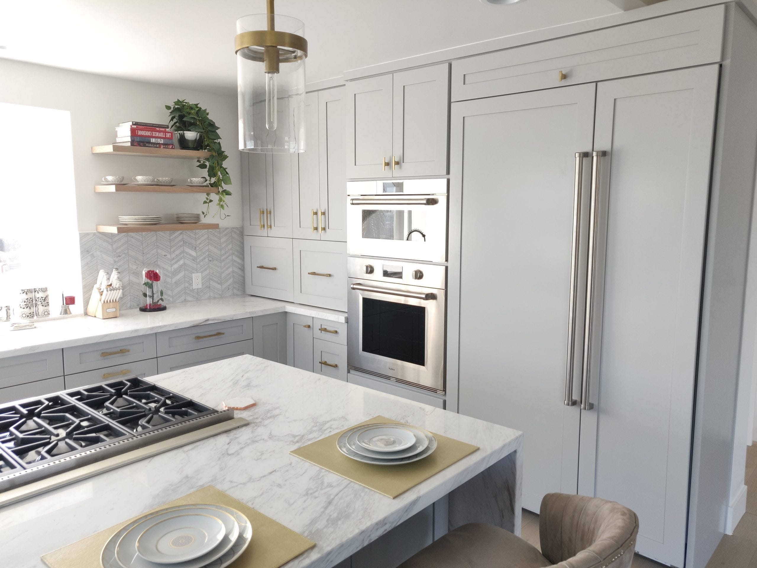 Transitional kitchen with gray cabinetry, marble island and built-in wall ovens