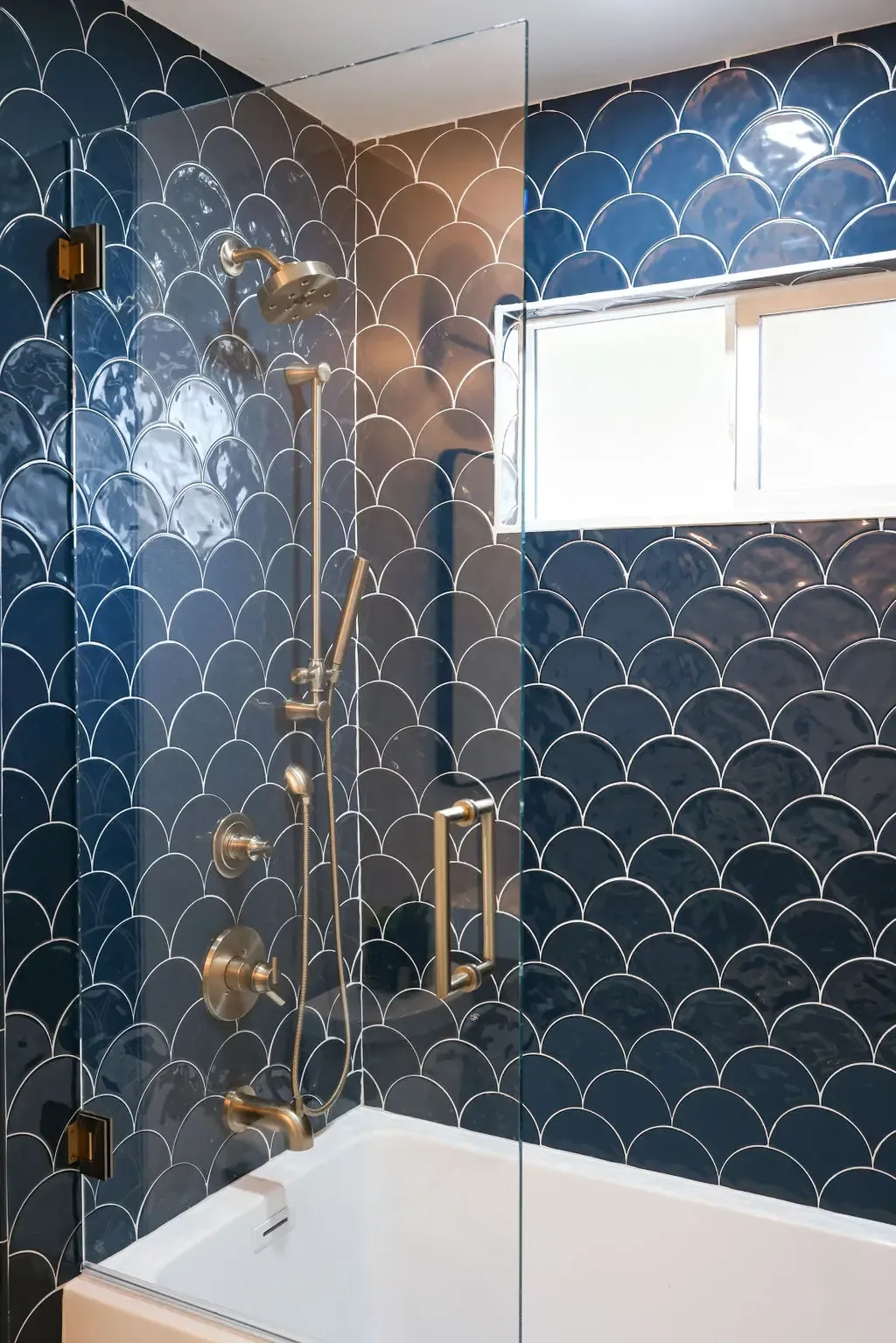 Tub and shower combo wrapped in glossy blue scallop tile with gold fittings