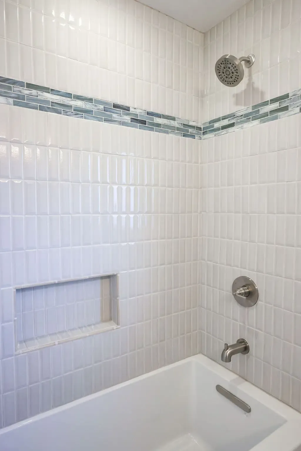 Tub-shower with stacked white tile, blue glass mosaic accent stripe, and recessed niche