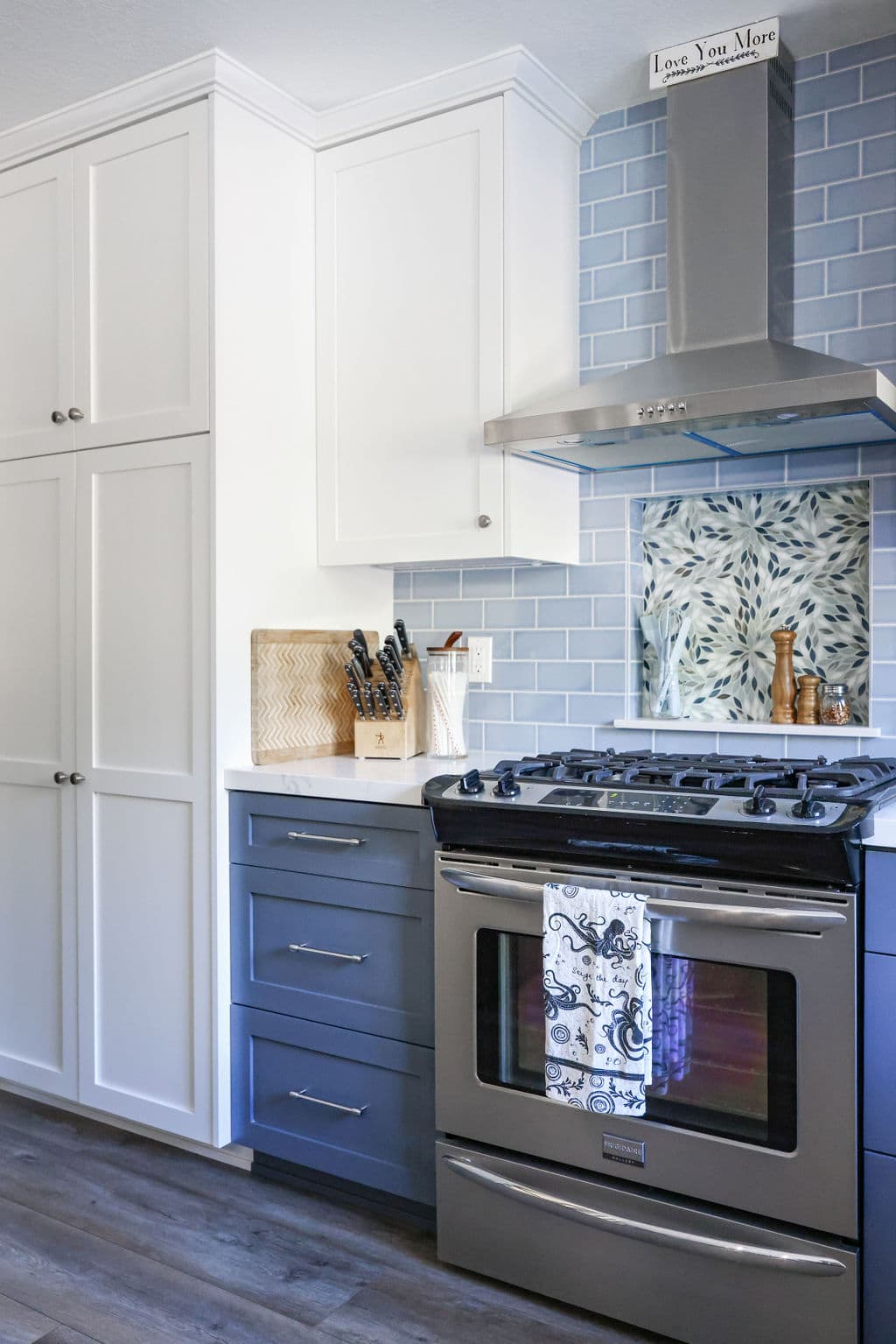 Two-tone kitchen with white and navy shaker cabinets, blue subway tile and stainless gas range