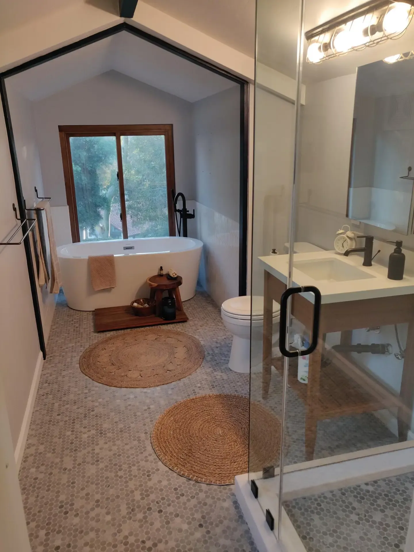 Vaulted bathroom with freestanding tub, glass shower and round jute floor mats