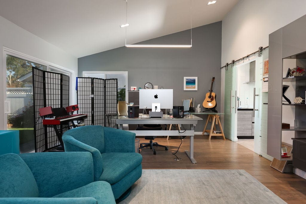 Vaulted-ceiling home office with gray walls, glass barn door and wood floors