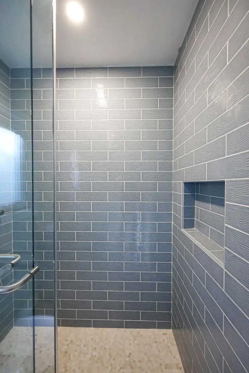 Walk-in glass shower clad in glossy blue subway tile with niche