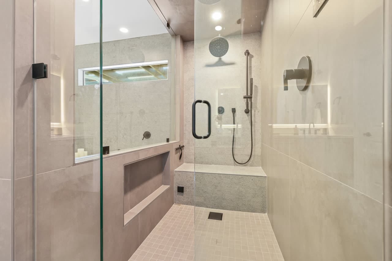 walk-in glass shower with large-format gray tile, bench and rain fixture