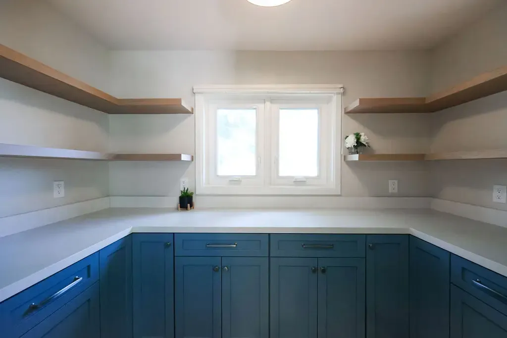 Walk-in pantry with deep blue cabinetry, white quartz counters, and floating wood shelves